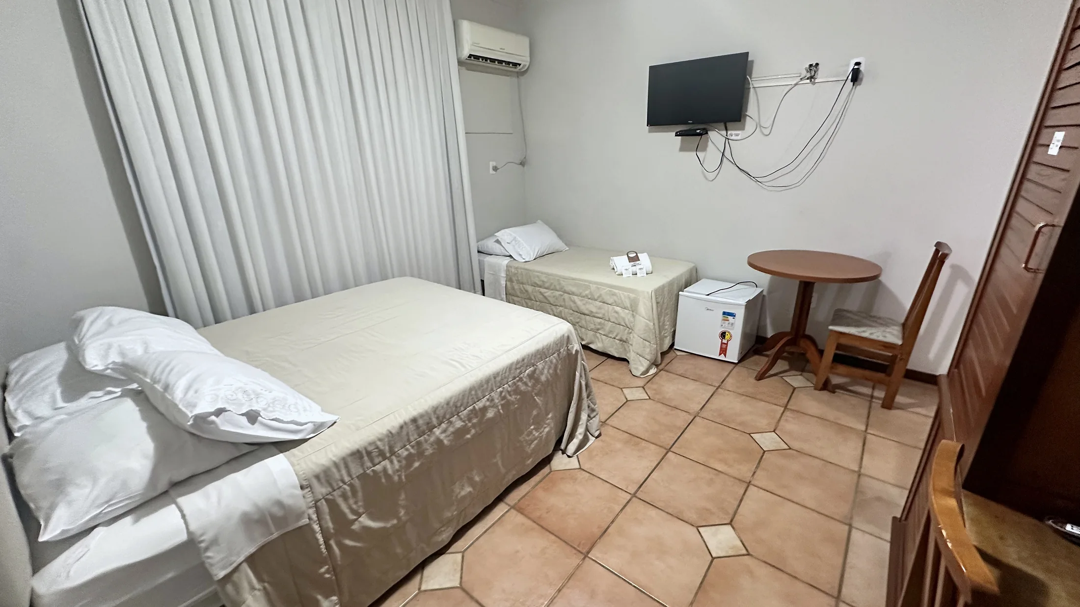 Quarto real do Hotel Beira Rio com camas, mesa, TV e frigobar